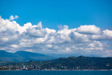 Mountains with the city against the blue sky with white clouds, at the bottom of the frame line of the sea