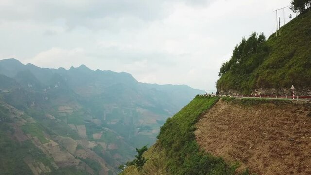 Drone shot of a winding road on the edge of an abrupt mountain at Ma Pi Leng Pass, Vietnam with mountains in the background. Hairpins on the edge of the mountains in South East Asia.