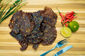 Jerky on wooden table, decoration with lemon, chili, and spoon