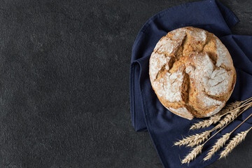 Loaf of sourdough bread with crispy crust on black background top view.