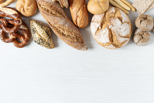 Assortment of baked bread and buns on white wooden background top view.