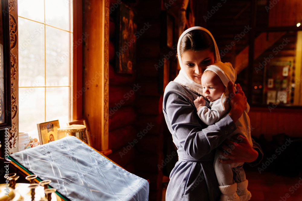 Wall mural beautiful mom in a headscarf with a small child in her arms in church. 