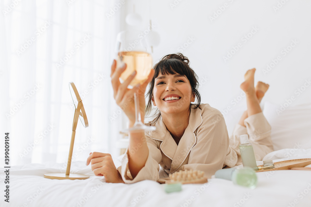 Wall mural Woman enjoying wine lying on bed at home