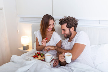Obraz na płótnie Canvas Young handsome man feeding attractive young woman in bed in the morning. Romantic breakfast for two. Love , care, relatioships. couple having healthy breakfast together in bed at home