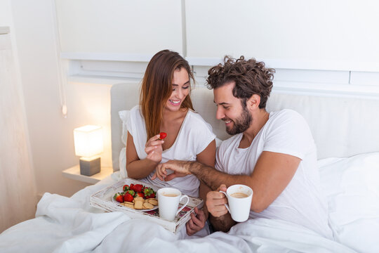 Young handsome man feeding attractive young woman in bed in the morning. Romantic breakfast for two. Love , care, relatioships. couple having healthy breakfast together in bed at home
