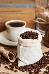 Cup of coffee and jute sack with raw grains on the table.