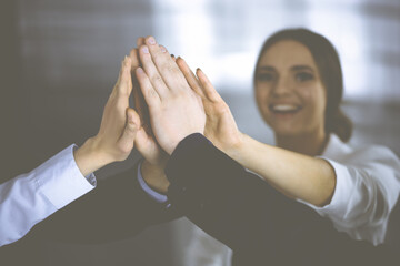 Young businesspeople are celebrating success of their project, standing in a modern office. Unknown businessmen are giving five to each other. Business success concept