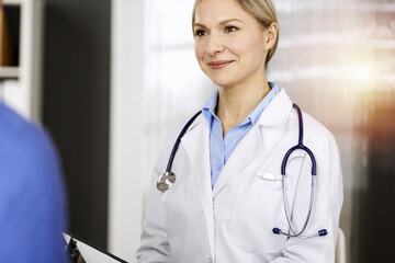 Friendly female doctor and patient man discussing current health examination while sitting in sunny...
