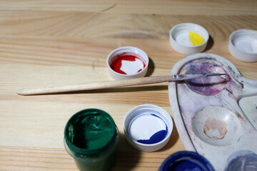 paints, brush and palette on the wooden table of novice artist close up
