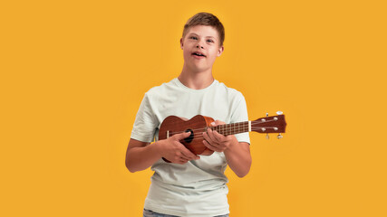 Teenaged disabled boy with Down syndrome having fun while playing ukulele, standing isolated over...