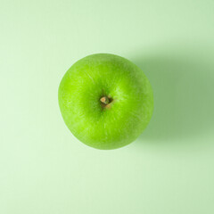 A green apple on a light green background. Flat lay view. Square size of photo.