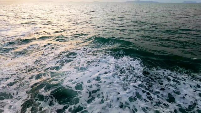 Aerial top view of calm ocean wave with white foam n green sea tide water surface reflaction of pastel goden pink sun light ray on yellow purple sunset sky background with mountain, 4k b-roll footage