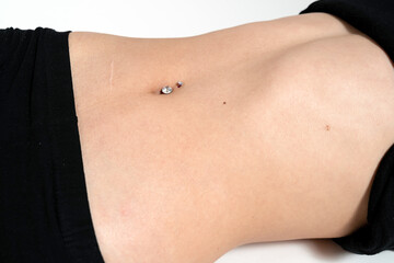 Belly button or navel piercing of young woman isolated on white.