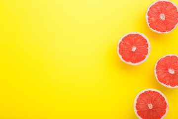 Halves of red grapefruits on bright yellow table background. Fresh fruits. Closeup. Empty place for text. Top down view.