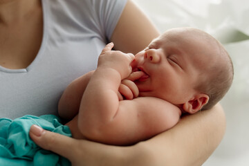 Young mother of a family brunette holds a newborn toddler in her arms - her tiny son in the bedroom at home
