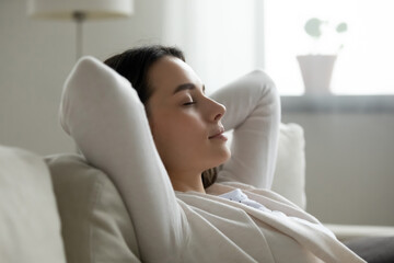 Close up peaceful young woman with hands behind head relaxing on cozy sofa, calm attractive girl taking nap, daydreaming or visualizing, leaning back on couch alone, spending lazy weekend