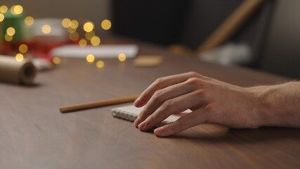man writes christmas gift list for holidays in notepad with a pencil under warm light in the evening