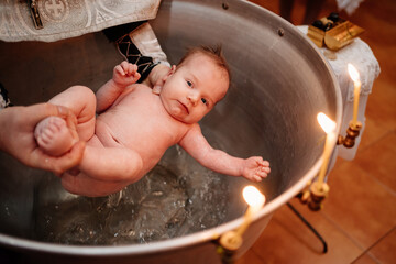 a child is lowered into the water in a font at a Christian baptism in the church