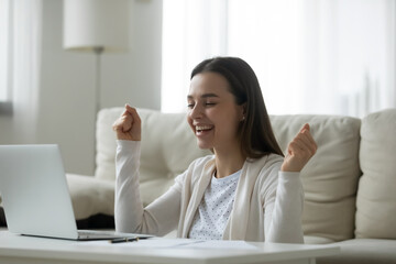 Overjoyed young woman looking at laptop screen, celebrating success, sitting at table in living room, happy excited girl reading good news in email, great sale shopping offer, exam results