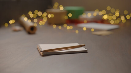 Notepad with pencil on walnut wood table with christmas lights on background