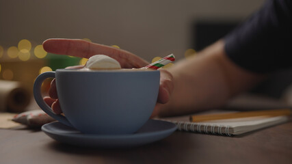 man drinking hot chocolate from blue cup in the evening making shopping list for holidays