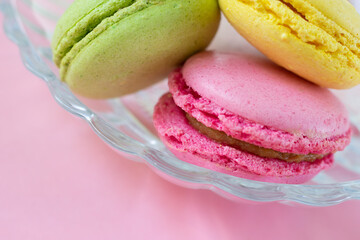 Close up photo of colorful almond round cookies with different interlayers in translucent glass plate on pink background. Macro food