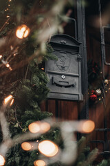 Old black vintage mailbox decorated with sprigs of fir for Christmas holidays. Old bricks house.