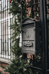 Old black vintage mailbox decorated with sprigs of fir for Christmas holidays. Old bricks house.