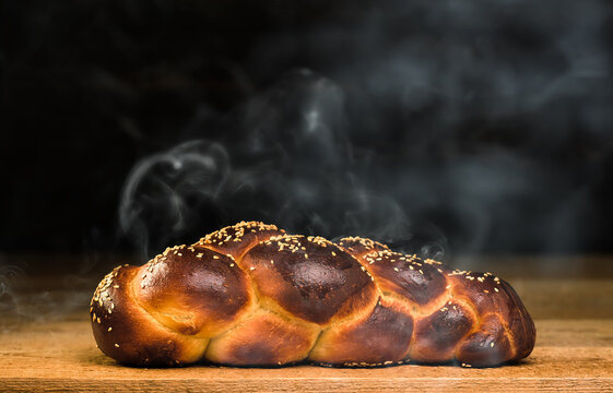 Freshly baked challah from the oven on a wooden table. Steam rises above the bread. Close-up, festive bread