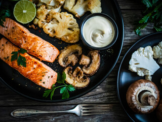 Roasted salmon steaks with fried cauliflower, fried brown champignons, lime and mayonnaise on wooden table
