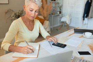 Stylish blonde middle aged female entrepreneur making investment plan, calculating finances at...