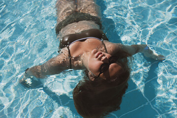 Fashion portrait of graceful cute girl in stylish sunglasses posing in the pool during holidays on luxury resort. Cheerful plus size teenage girl enjoying. happy, positive emotion, summer style.