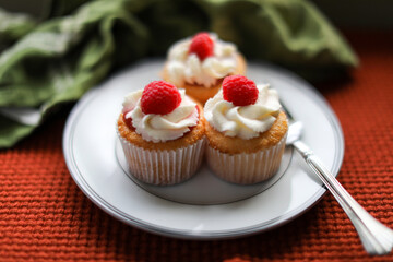 Angel food cupcakes with raspberry jam, whipped cream frosting and topped with a fresh raspberry.