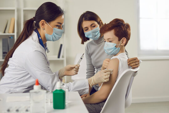 Woman pediatrician in medical protective mask wiping arm of teen boy patient before vaccination