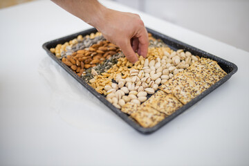 Male hand picking nuts from a black tray with seeds and nuts