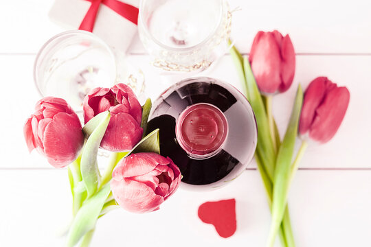 Holiday concept. Tulips with gifts and wine on a white table.