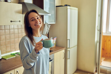 Fototapeta na wymiar Young cheerful and happy woman is preparing tasty tea at her kitchen at home