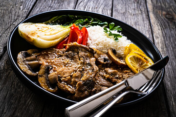 Fried pork steaks with lemon, basmati rice and steamed pak choi cabbage served on wooden table
