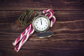 Two red white candy canes and pocket watch on brown wooden surface