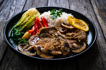 Fried pork steaks with lemon, basmati rice and steamed pak choi cabbage served on wooden table

