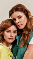 Close up portrait of two attractive young girls, twin sisters looking at camera, posing together isolated over light background