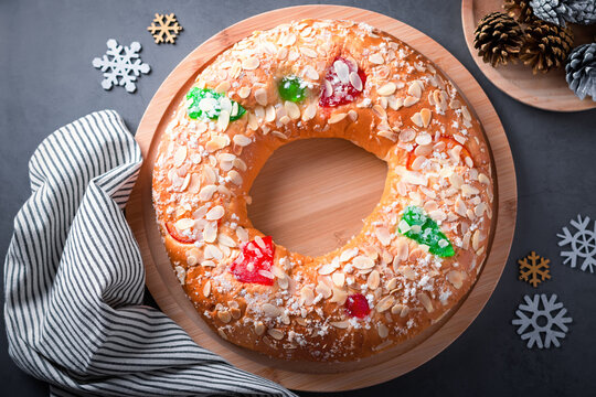 Traditional Epiphany cake Roscon de Reyes on grey stone table top with small Christmas tree and decoration closeup, top view