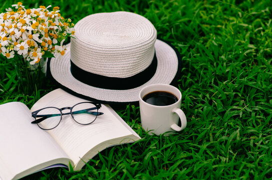 Leisure in morning at garden with coffee, book , hat and flowers on the lawn..