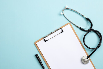 Blank medical clipboard with stethoscope on blue background.