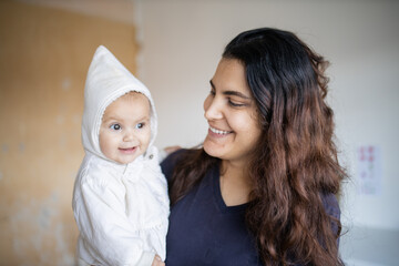 Happy woman holding her adorable baby in white clothing