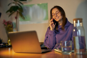 Young cheerful confident and happy freelancer woman is working on laptop at home in the evening