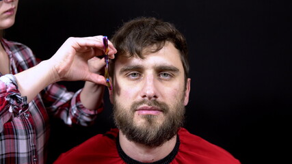 A man in a hairdressing salon a woman master cuts her hair on a black background