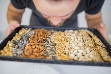 Man holding and smelling a black tray of nuts and seeds