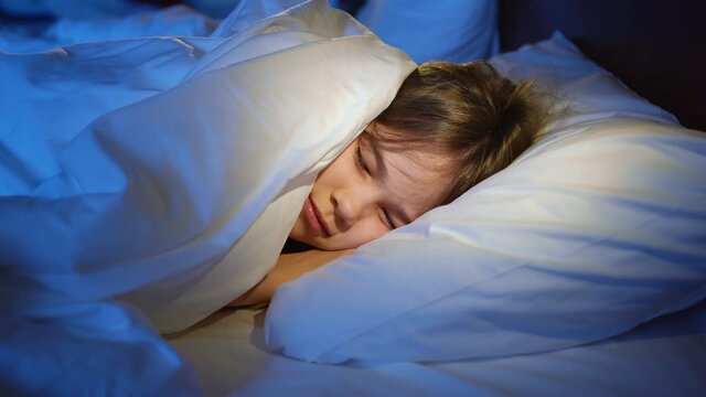 A girl naps in bed in her room, sees a terrible dream and winces in her sleep.