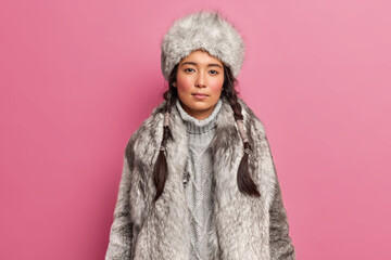 Portrait of arctic woaman with two pigtails dresses for cold climate wears grey fur coat and hat...